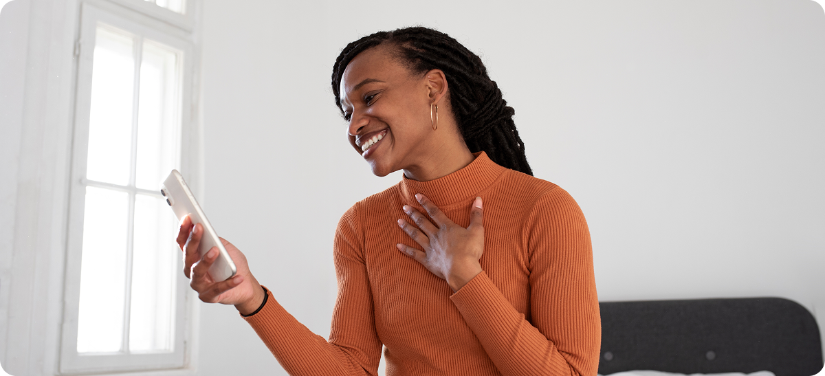 image of a woman in an orange sweater smiling at her phone